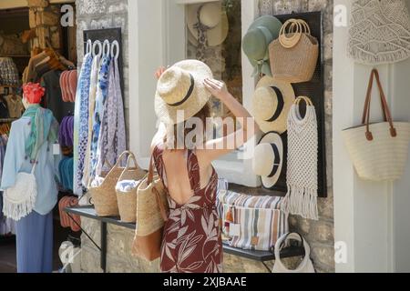 Eine junge Frau, die im Souvenirladen einen Strohsommerhut auswählt Stockfoto