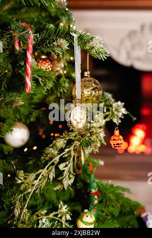 Eine Nahaufnahme eines alten Weihnachtsschmucks, der an einem verzierten Baum hängt, mit einem Kamin im Hintergrund Stockfoto