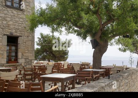 Holztische und -Stühle im Straßencafé in der kleinen Mediteeraner Stadt, an heißem Sommertag, keine Leute Stockfoto