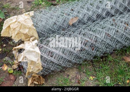 Verzinktes Metallgeflecht in Rollen auf dem Gras. Für die Montage des Zauns werden Baumaterialien vorbereitet. Stockfoto