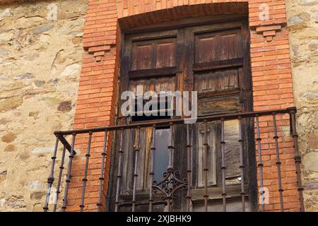 Ein verwitterter Holzbalkon mit einem rostigen Eisengeländer und einer einsamen Taube am Rand, mit Blick auf die bezaubernden Straßen von Astorga, Spanien. Stockfoto