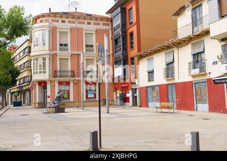 Astorga, Spanien - 3. Juni 2023: Ein ruhiger Platz in Astorga, Spanien, mit einer Bronzeskulptur, farbenfrohen Gebäuden, einer schattigen Bank und sonnigen Schatten auf Kopfsteinpflaster Stockfoto