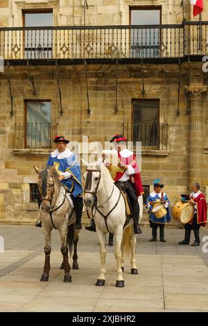 Astorga, Spanien - 3. Juni 2023: Zwei Männer zu Pferd, gekleidet in napoleonischer Ära, reiten durch einen Stadtplatz. Dahinter spielen zwei Musiker Schlagzeug Stockfoto