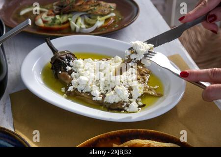 Frau isst geröstete Auberginen gefüllt mit Fetakäse in Olivenöl, mediterraner Sommerstil Stockfoto