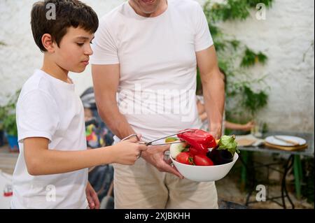 Vater und Sohn bereiten frisches Gemüse für eine Mahlzeit im Freien zu. Die Szene spielt in einer ungezwungenen, familienfreundlichen Umgebung, in der das Binden und das Hervorheben betont wird Stockfoto