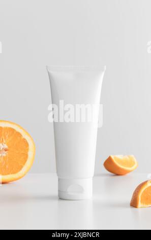 Weiße Tube Creme mit Orangen auf einem weißen Tisch. Stockfoto