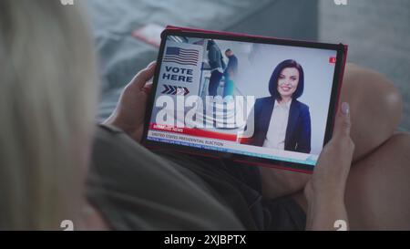 Der Tablet-Bildschirm zeigt Fernsehnachrichten mit weiblicher Nachrichtensprecherin. Kaukasische Frau, die Nachrichten über US-Präsidentschaftswahlen mit einem digitalen Tablet auf dem Sofa ansieht. Nahaufnahme. Stockfoto