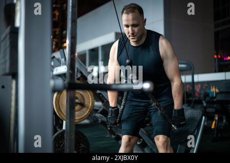 Ein Mann in einem schwarzen Tanktop und Shorts macht eine Lat-Pulldown-Übung in einem Fitnessstudio. Stockfoto