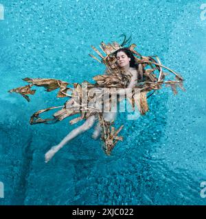 Eine Frau schwimmt friedlich in einem Pool, geschmückt mit getrockneten Bananenblättern. Der Kontrast des leuchtenden blauen Wassers und der natürlichen Erdtöne erzeugt ein s Stockfoto