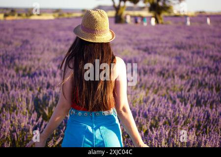 Romantische, fröhliche junge Frau mit Strohhut läuft durch ein Lavendelfeld mit lila Blumen. Menschen in blühender Natur im Sommer. Stockfoto