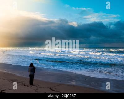 Frau mit Blick aufs Meer in dramatischer Strandszene Stockfoto