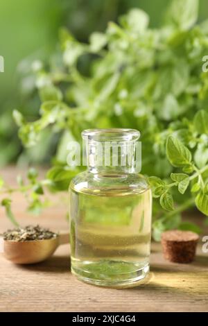 Ätherisches Öl in der Flasche, Löffel mit trockenem Kraut und Oregano-Zweigen auf Holztisch, Nahaufnahme Stockfoto