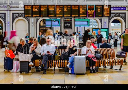 Passagiere sitzen und warten auf ihre Züge am Bahnhof Paddington. Elektronische Abfahrtstafeln zeigen die Zeiten der Abfahrten an, während die Menschen herumlaufen. Stockfoto