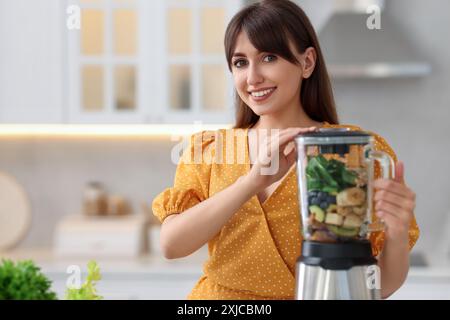 Junge Frau, die leckeren Smoothie mit Mixer in der Küche macht. Leerzeichen für Text Stockfoto