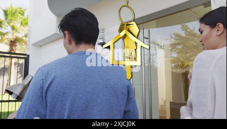Bild von goldenem Hausschlüssel und Schlüsselanhänger über glückliches, vielfältiges Paar, das in ein neues Zuhause zieht Stockfoto