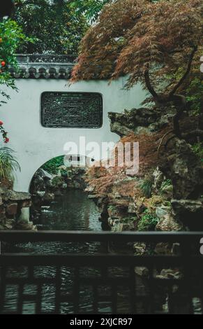 Ein ruhiger Bach fließt unter einer weißen Bogenbrücke in einem üppigen, grünen Garten. Die Brücke verfügt über ein dekoratives Eisenfenster und ist von großen umgeben Stockfoto