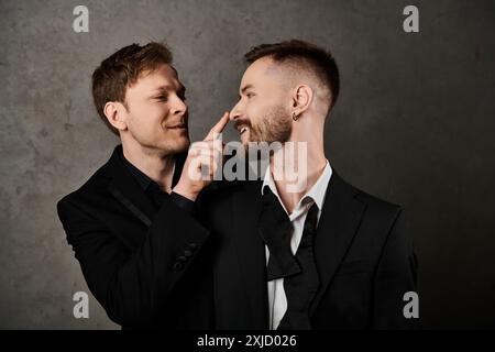 Zwei Männer in eleganten Anzügen wirken spielerisch vor grauem Hintergrund. Stockfoto