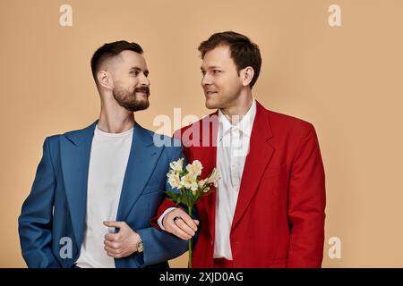 Zwei Männer in stylischen Anzügen sehen sich vor einem weichen Hintergrund liebevoll an. Stockfoto