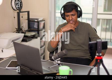 Junger Mann, der in die Erstellung von Inhalten für seinen Kanal für technische Rezensionen vertieft ist, umgeben von Gadgets. Stockfoto