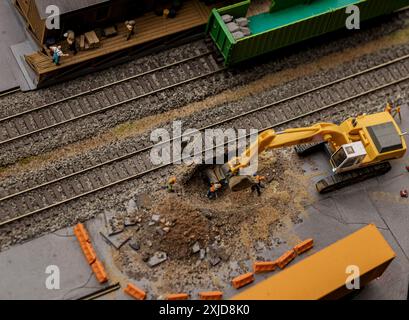 Hochbau. Draufsicht Miniaturbauer bei der Arbeit und Miniaturbagger. Kleine Spielzeugbaugeräte und Arbeiter vor Ort. Stockfoto