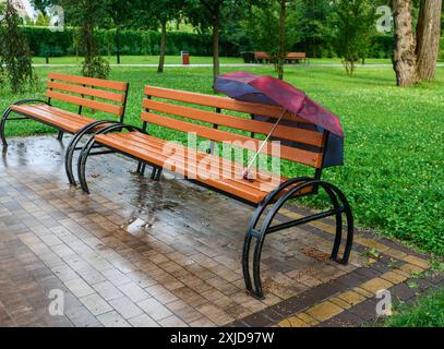 Ein vergessener, geöffneter Schirm auf einer Bank nach Regen im Stadtpark. Stockfoto