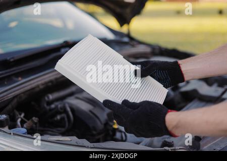 Der Automechaniker hält einen neuen Innenraumluftfilter, um den alten Filter zu ersetzen. Stockfoto