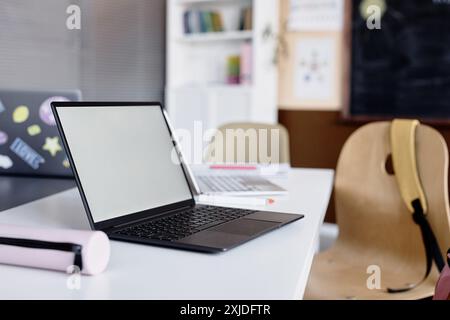 Seitenansicht des leeren Modellbildschirms des offenen Laptops auf dem Schreibtisch im leeren Klassenzimmer, Kopierraum Stockfoto