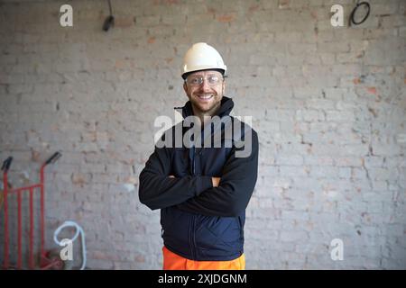 Porträt eines jungen lächelnden Mannes, der auf der Baustelle mit der Hand gekreuzt steht. Stockfoto