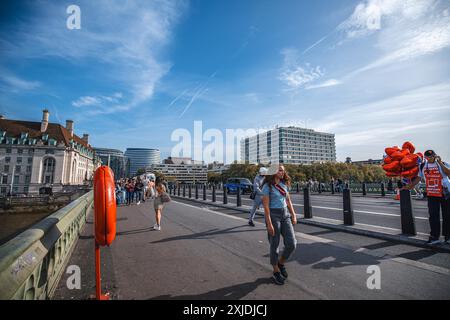 London, UK - 9. Oktober 2023 : Eine junge Frau spaziert entlang einer Londoner Straße, mit der Themse und dem St. Thomas' Hospital im Hintergrund, unter einem b Stockfoto
