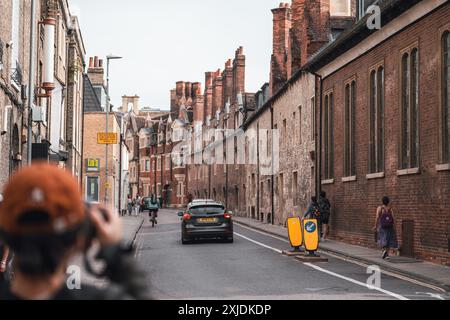 Cambridge, UK - 08. Oktober 2023 : Blick auf eine enge Straße in Cambridge, Großbritannien, gesäumt von historischen Backsteinhäusern. Ein Auto fährt vorbei, ein Radfahrer ist abgehauen Stockfoto