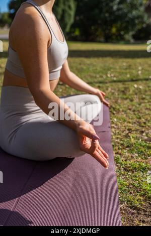 Eine vertikale Aufnahme einer Frau, die Yoga praktiziert, sitzt in einer Meditationsposition mit Mudra-Händen im Park an einem sonnigen Tag, mit unscharfem Hintergrund Stockfoto