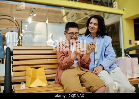 Eine Mutter und ihr Sohn mit Down-Syndrom lachen, während sie gemeinsam in der Mall auf ein Telefon schauen. Stockfoto