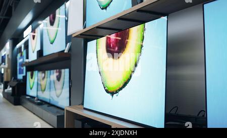 Aufnahme des Retail Electronics Stores mit beeindruckender Wand der neuesten Fernseher und farbenfrohen Makro-Demo-Aufnahmen. Auswahl an hochwertigen Fernsehgeräten im zeitgenössischen Storefront Space Stockfoto