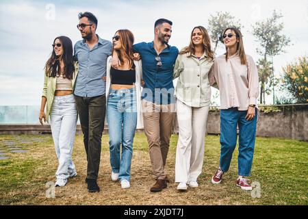 Verschiedene Gruppen von Millennial-Freunden, die an einem sonnigen Tag zusammen spazieren gehen. Sechs junge Menschen genießen Freizeit im Freien und zeigen Freundschaft und Vielfalt Stockfoto