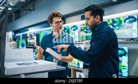 Junge, multiethnische Kunden beraten mit einem Verkäufer für Home Electronics Store. Ein stilvoller Mann ist am Kauf eines Smartphones interessiert. Kunde sucht ein neues Mobiltelefon in einem modernen Shop Stockfoto