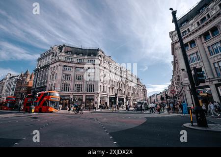 London, UK - 10. Oktober 2023 : Eine belebte Straße in London mit roten Doppeldeckerbussen, Fußgängern, die die Straße überqueren, und verzierten Gebäuden. Stockfoto