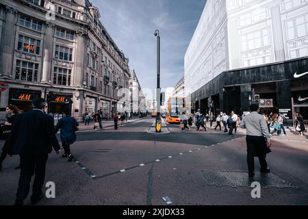 London, UK - 10. Oktober 2023 : Menschen überqueren die Straße vor einem HM-Geschäft in der Londoner Regent Street. Ein Doppeldeckerbus wird im Backgr angehalten Stockfoto