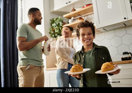 Ein kleiner Junge hält zwei Teller mit Essen im Hintergrund mit seinen Eltern. Stockfoto