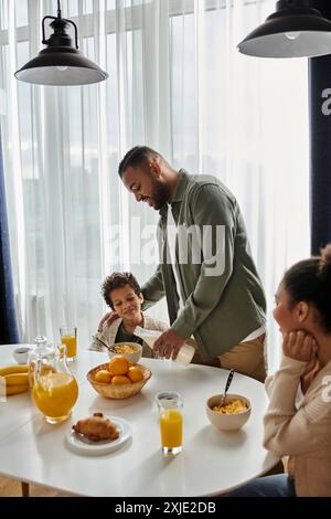 Ein Mann steht über einem Tisch mit viel Essen, neben Sohn und Frau. Stockfoto