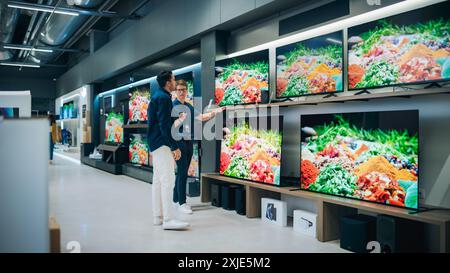 Junge, multiethnische Kunden beraten mit einem Verkäufer für Home Electronics Store. Ein stilvoller Mann möchte einen Flachbildfernseher kaufen. Kunden kaufen ein neues Fernsehgerät im Modern Shop Stockfoto