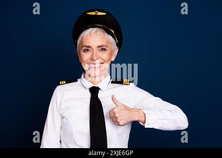 Foto von der schönen Rentnerin Frau professionellem kommerziellen Piloten Daumen oben gekleidete Pilotenuniform isoliert auf dunkelblauem Hintergrund Stockfoto