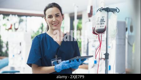 Krankenschwester Hält Tablet-Computer Und Überprüft Den Blutbeutel Im Spendenzentrum. Professionelle Kaukasierin Schaut In Die Kamera Und Lächelt Fröhlich Und Lädt Spender Ein, Leben Zu Retten. Stockfoto