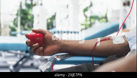 Nahaufnahme der Hand eines männlichen Blutspenders mit angebrachtem Katheter. Schwarzer Mann Hält Einen Herzförmigen Roten Ball, Um Blut Durch Den Schlauch In Den Beutel Zu Pumpen. Spende Für Organtransplantationspatienten. Stockfoto