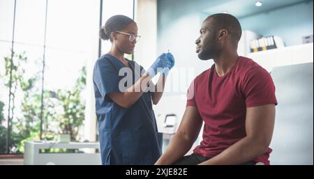 Afroamerikaner Sitzt Auf Dem Stuhl Im Krankenhaus Und Bekommt Seinen Windpocken-Impfstoff. Die professionelle schwarze Krankenschwester führt eine Injektion durch und setzt Ein Pflaster auf. Public Healthcare-Konzept. Stockfoto