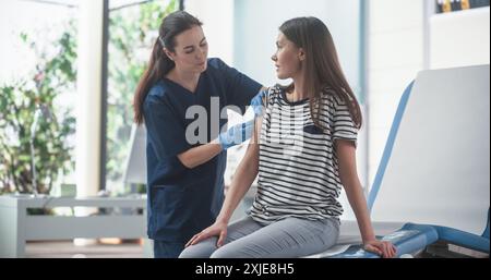 Glückliche kaukasische Frau, die auf dem Stuhl im Bright Hospital sitzt und ihren MMR-Impfstoff bekommt. Die professionelle Krankenschwester führt eine Injektion durch und setzt Ein Pflaster auf. Public Healthcare-Konzept. Stockfoto