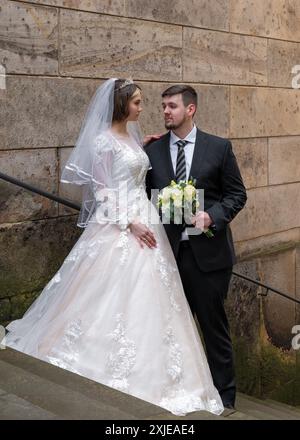 Braut und Bräutigam. Die Braut trägt ein langes, sehr schönes Hochzeitskleid, hält einen Blumenstrauß, während sich die jungen Leute anschauen Stockfoto