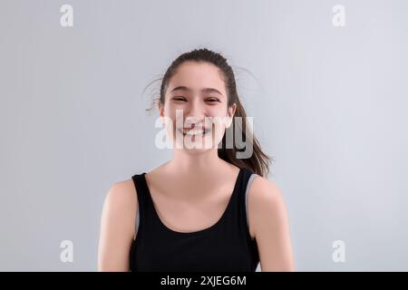 Glückliche junge Frau lächelt vor einem weißen Hintergrund hell und strahlt Freude und Positivität aus mit ihrem ansteckenden Ausdruck der Zufriedenheit Stockfoto