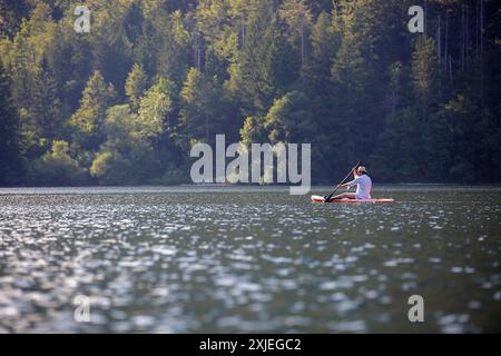 Touristen mit Strohhut paddeln auf einem Paddelbrett vor Sonnenuntergang an einem schönen Sommertag auf dem Bohinj-See im Triglav-Nationalpark in Slowenien Stockfoto