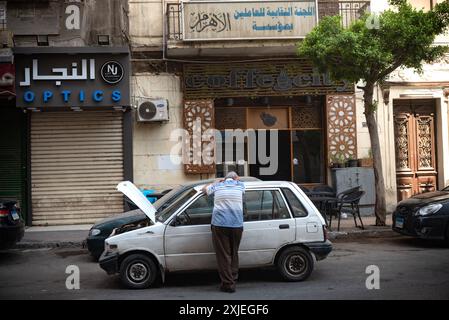 Kairo, Ägypten. 24. Juni 2024 ein ägyptischer Mann wartet in der Sommerhitze der Innenstadt von Kairo an seinem kaputten Auto. Stockfoto