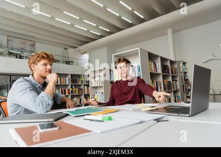 Zwei junge männliche Studenten sitzen an einem Tisch und arbeiten an einem Laptop. Stockfoto